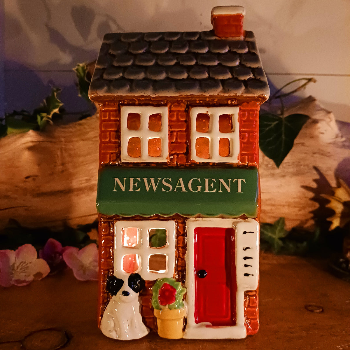 Bring a touch of village charm to your home with the Village Pottery Newsagent Tealight Holder. Beautifully designed as a traditional little village newsagent, this charming ceramic tealight holder features a warm red-brick façade, textured cream tiled roof and cheerful bright red front door.
