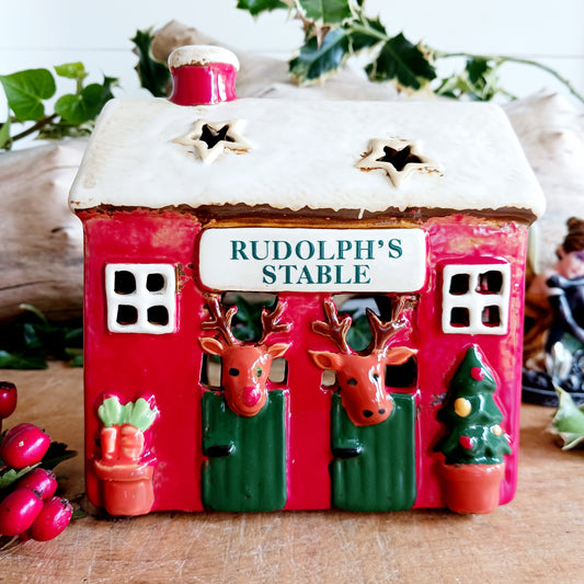 Bring a touch of festive village charm to your home with the Village Pottery Xmas Rudolph’s Stable Tealight Holder. This delightful ceramic Christmas decoration is designed as a quaint little stable, featuring a snowy roof, traditional green doors and charming reindeer detailing.