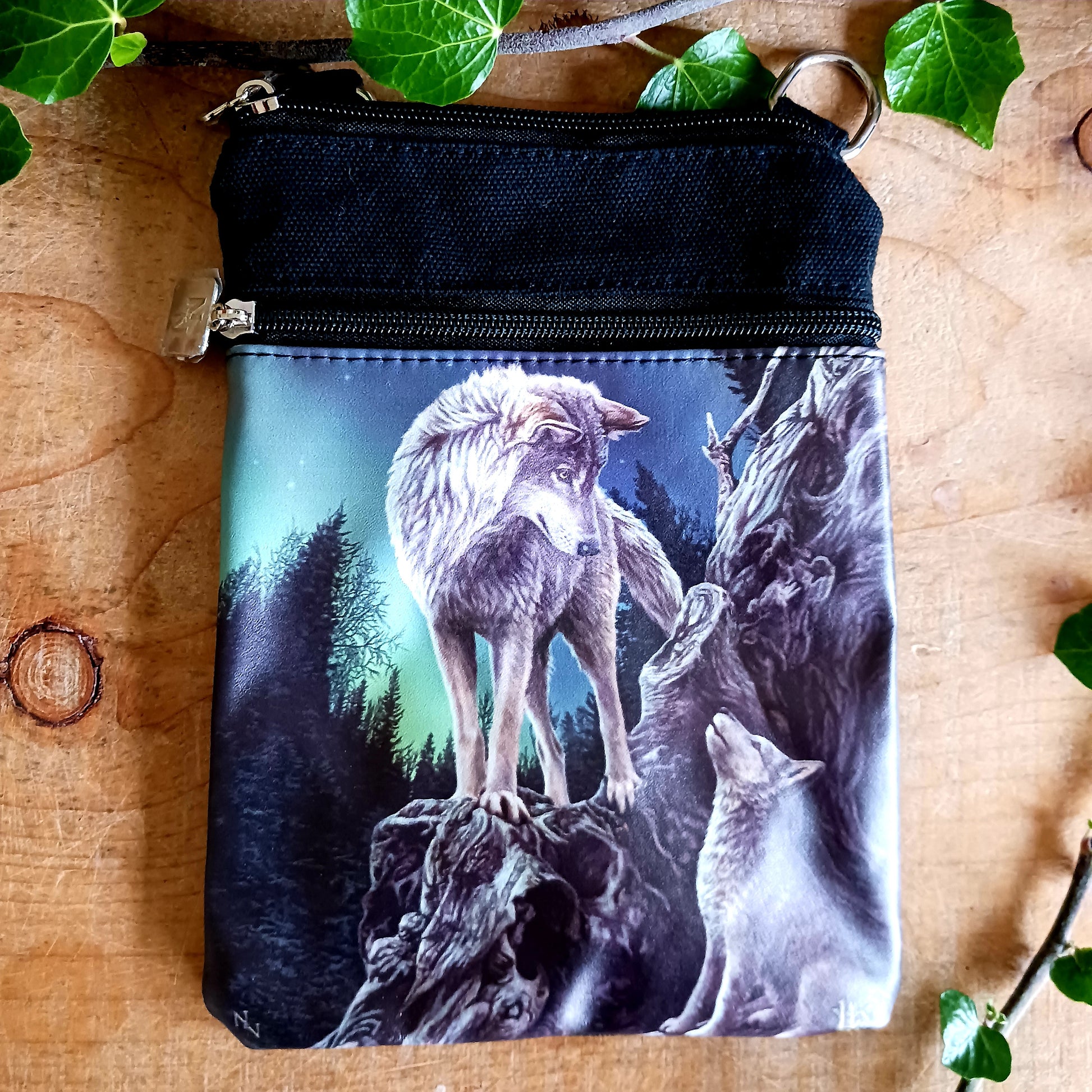 Step into a world of magic, guidance, and untamed wilderness with this stunning Lisa Parker Wolf &amp; Pup Shoulder Bag, from Nemesis Now. Featuring enchanting artwork from the renowned fantasy and wildlife artist Lisa Parker, this bag captures a tender moment beneath a starlit sky as a majestic wolf watches protectively over their pup beneath the glowing aurora borealis.