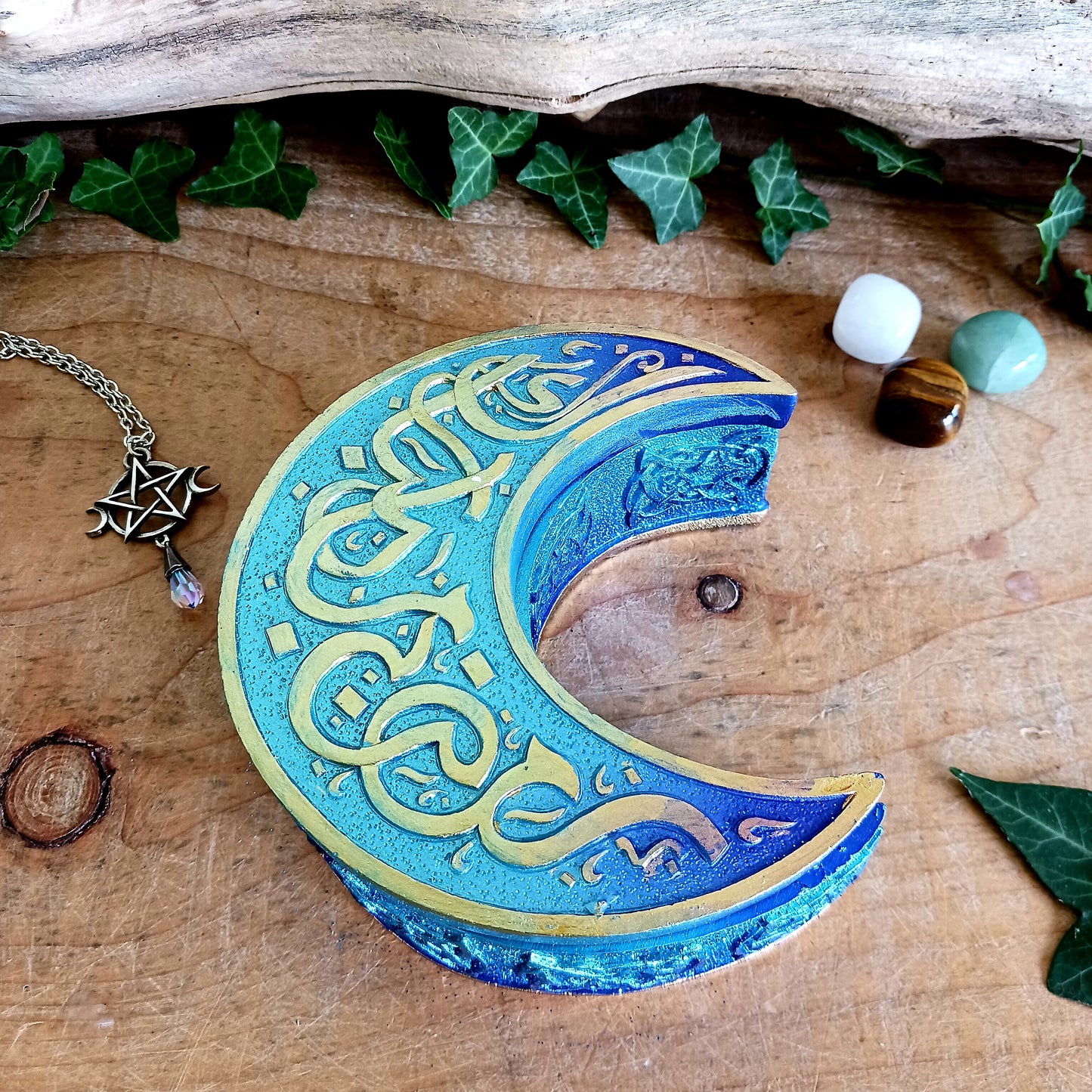 Safely store your small crystals, jewellery, or magical keepsakes in this enchanting&nbsp;Blue Crescent Moon Trinket Box. Crafted from durable cold-cast resin, this Wiccan-inspired box is shaped like a crescent moon and features a fully removable lid. The raised lid design showcases curled silver ribbons set against a deep blue background, framed with a matching border. Celtic knotwork patterns adorn the sides, adding a mystical charm.