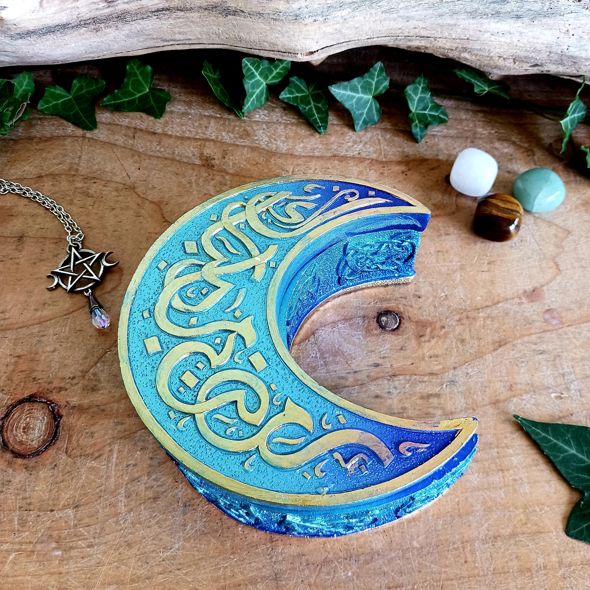 Safely store your small crystals, jewellery, or magical keepsakes in this enchanting&nbsp;Blue Crescent Moon Trinket Box. Crafted from durable cold-cast resin, this Wiccan-inspired box is shaped like a crescent moon and features a fully removable lid. The raised lid design showcases curled silver ribbons set against a deep blue background, framed with a matching border. Celtic knotwork patterns adorn the sides, adding a mystical charm.