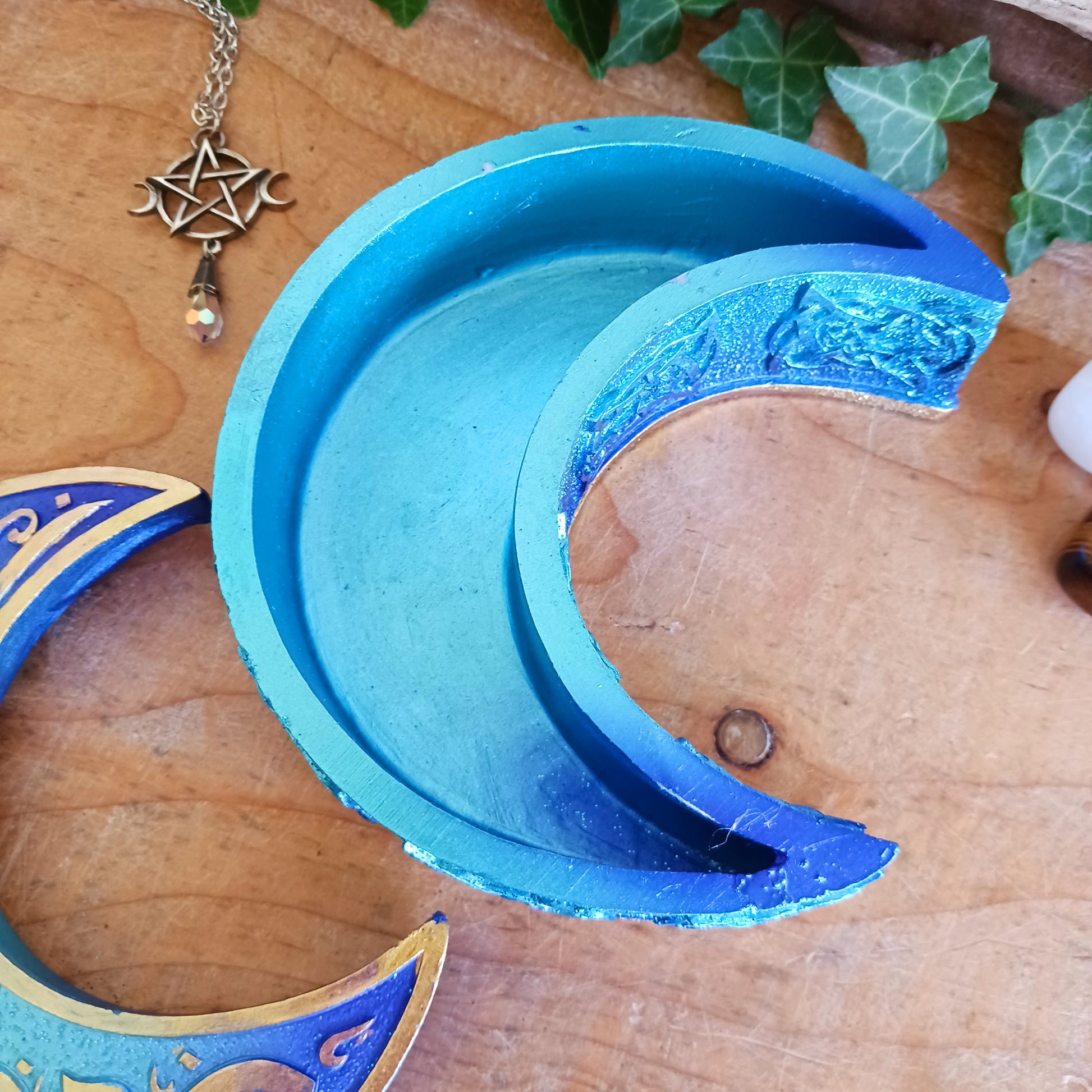 Safely store your small crystals, jewellery, or magical keepsakes in this enchanting&nbsp;Blue Crescent Moon Trinket Box. Crafted from durable cold-cast resin, this Wiccan-inspired box is shaped like a crescent moon and features a fully removable lid. The raised lid design showcases curled silver ribbons set against a deep blue background, framed with a matching border. Celtic knotwork patterns adorn the sides, adding a mystical charm.