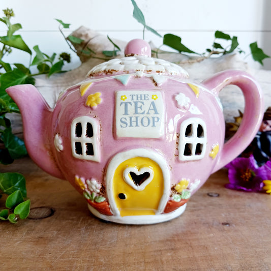 Add a sprinkle of charm to your home with this adorable Village Pottery ceramic tealight holder, beautifully designed as a whimsical pink teapot transformed into a cosy village tea shop. Featuring cottage-style windows, colourful bunting, pretty floral details and a welcoming heart-shaped doorway, this delightful decorative piece brings a touch of storybook magic to any room.