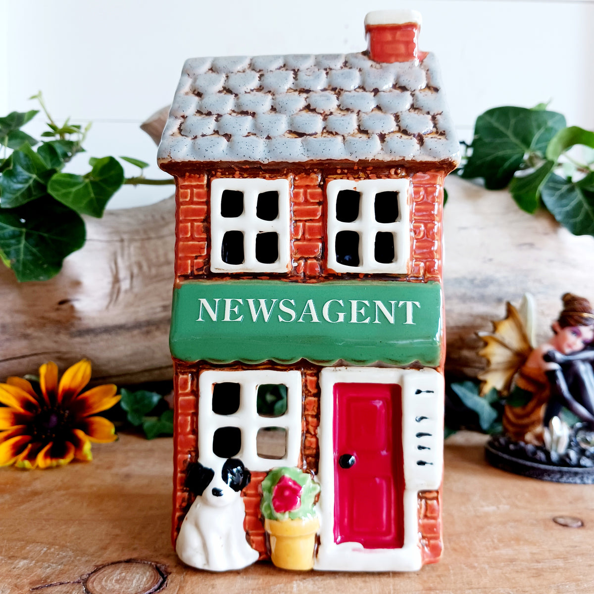 Bring a touch of village charm to your home with the Village Pottery Newsagent Tealight Holder. Beautifully designed as a traditional little village newsagent, this charming ceramic tealight holder features a warm red-brick façade, textured cream tiled roof and cheerful bright red front door.