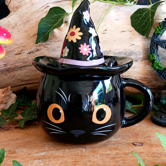 Add a spellbinding touch to your tea or coffee ritual with this groovy ceramic lidded mug, featuring an adorable cat wearing a whimsical witch hat adorned with a funky floral design.