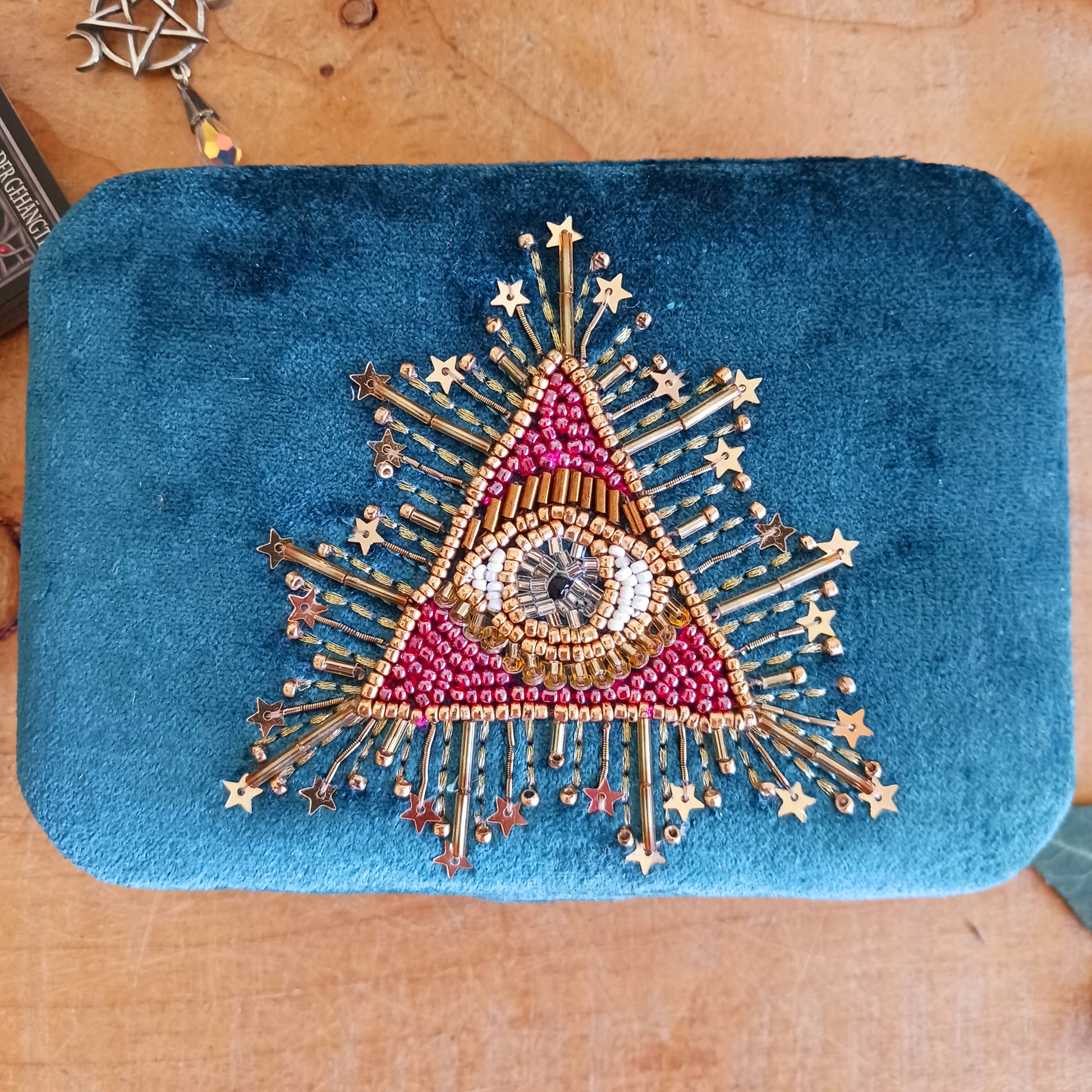Add elegance and mystique to your collection with this finely embroidered jewellery and tarot box. Made in India and crafted from soft velvet in a rich blue hue, this piece is adorned with intricate embroidery and ornamental beads for a touch of luxury. Perfect for storing jewellery, tarot cards, crystals, or other cherished items, its small strap and button closure keep your treasures secure.