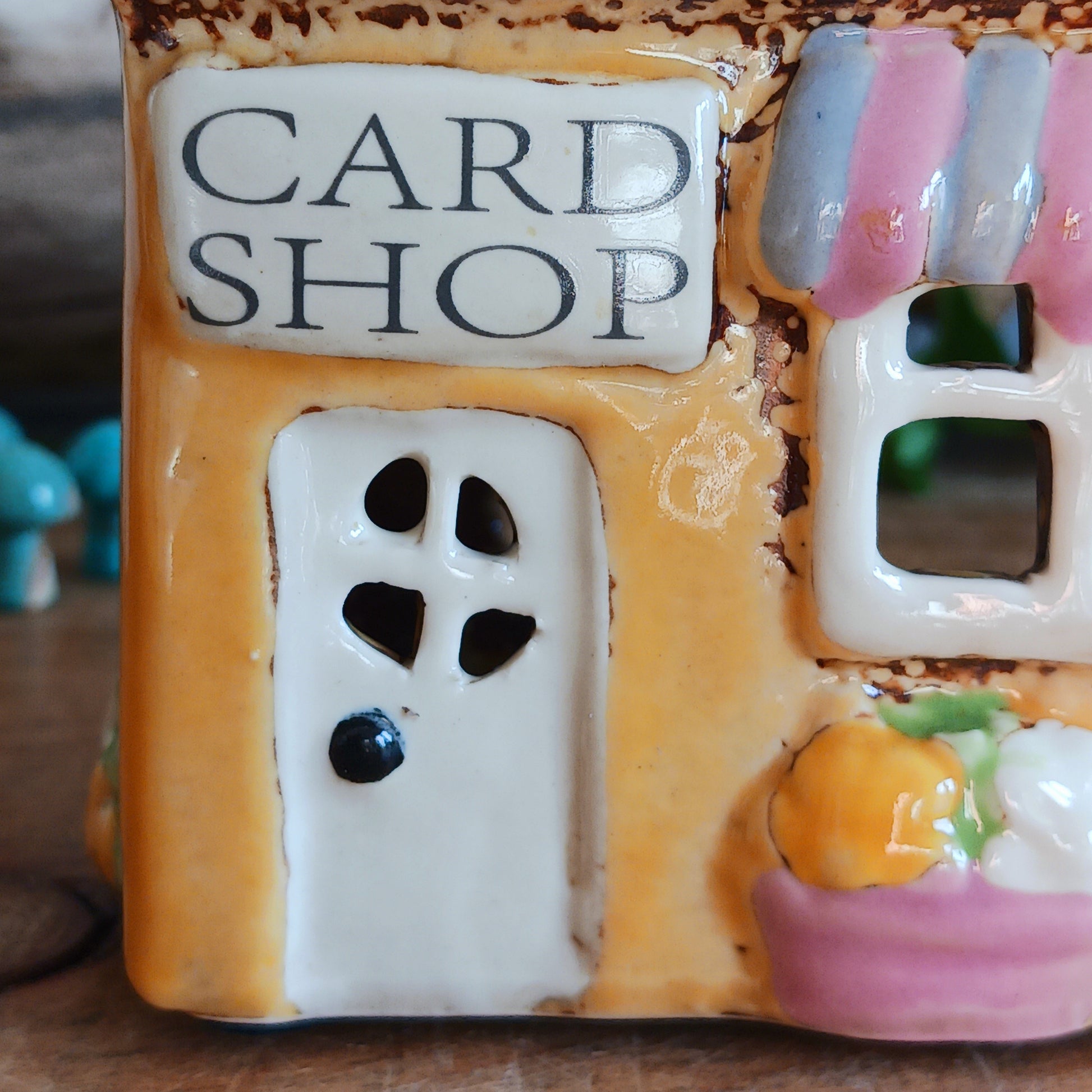 Add a whimsical touch to your décor with the Cards &amp; Gifts Tealight Holder from the Village Pottery Collection. Inspired by the charm of a cozy card shop in a quaint village, this ceramic piece features intricate detailing, from its bunting roof to its delicate windows. Perfect as a tealight holder or simply as a decorative ornament, it brings warmth and character to any space.