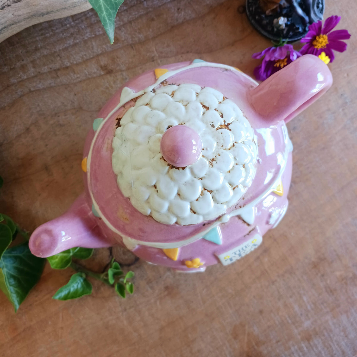 Add a sprinkle of charm to your home with this adorable Village Pottery ceramic tealight holder, beautifully designed as a whimsical pink teapot transformed into a cosy village tea shop. Featuring cottage-style windows, colourful bunting, pretty floral details and a welcoming heart-shaped doorway, this delightful decorative piece brings a touch of storybook magic to any room.