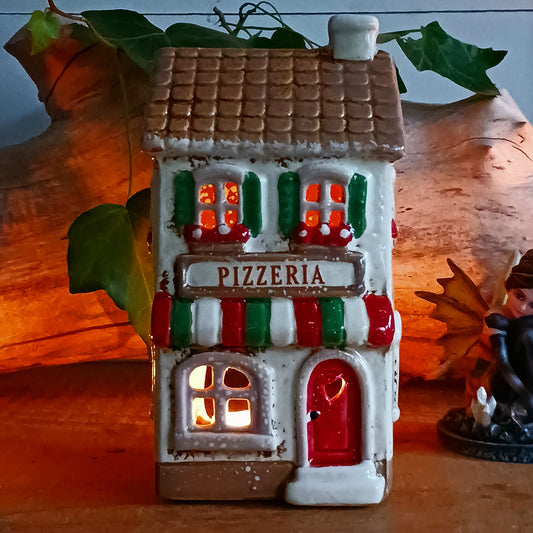 Bring a little taste of Italy into your home with this charming Village Pottery Pizzeria Tealight Holder. Designed as a delightful two-storey Italian village building, this cream pottery house features a brown tiled roof, chimney, green shutters, red flower boxes and colourful red and green striped awnings.