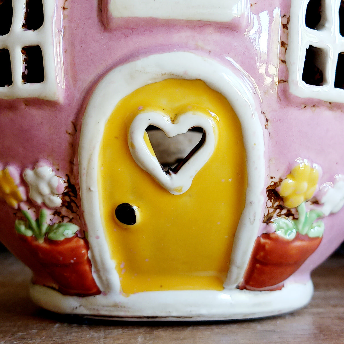 Add a sprinkle of charm to your home with this adorable Village Pottery ceramic tealight holder, beautifully designed as a whimsical pink teapot transformed into a cosy village tea shop. Featuring cottage-style windows, colourful bunting, pretty floral details and a welcoming heart-shaped doorway, this delightful decorative piece brings a touch of storybook magic to any room.
