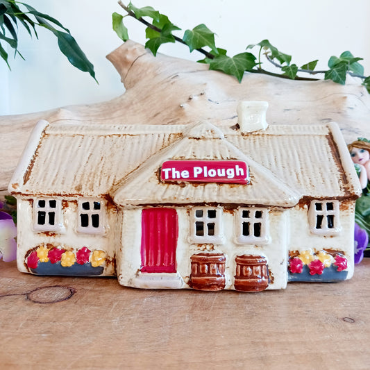 A hearth-lit gathering place where candlelight flickers like laughter carried on the evening air, the Croft Plough Pub brings rustic enchantment to your village scene. This Shudehill Village Pottery tealight house is crafted from ceramic, casting a warm, inviting glow through its windows to evoke comfort, connection, and quiet magic.
