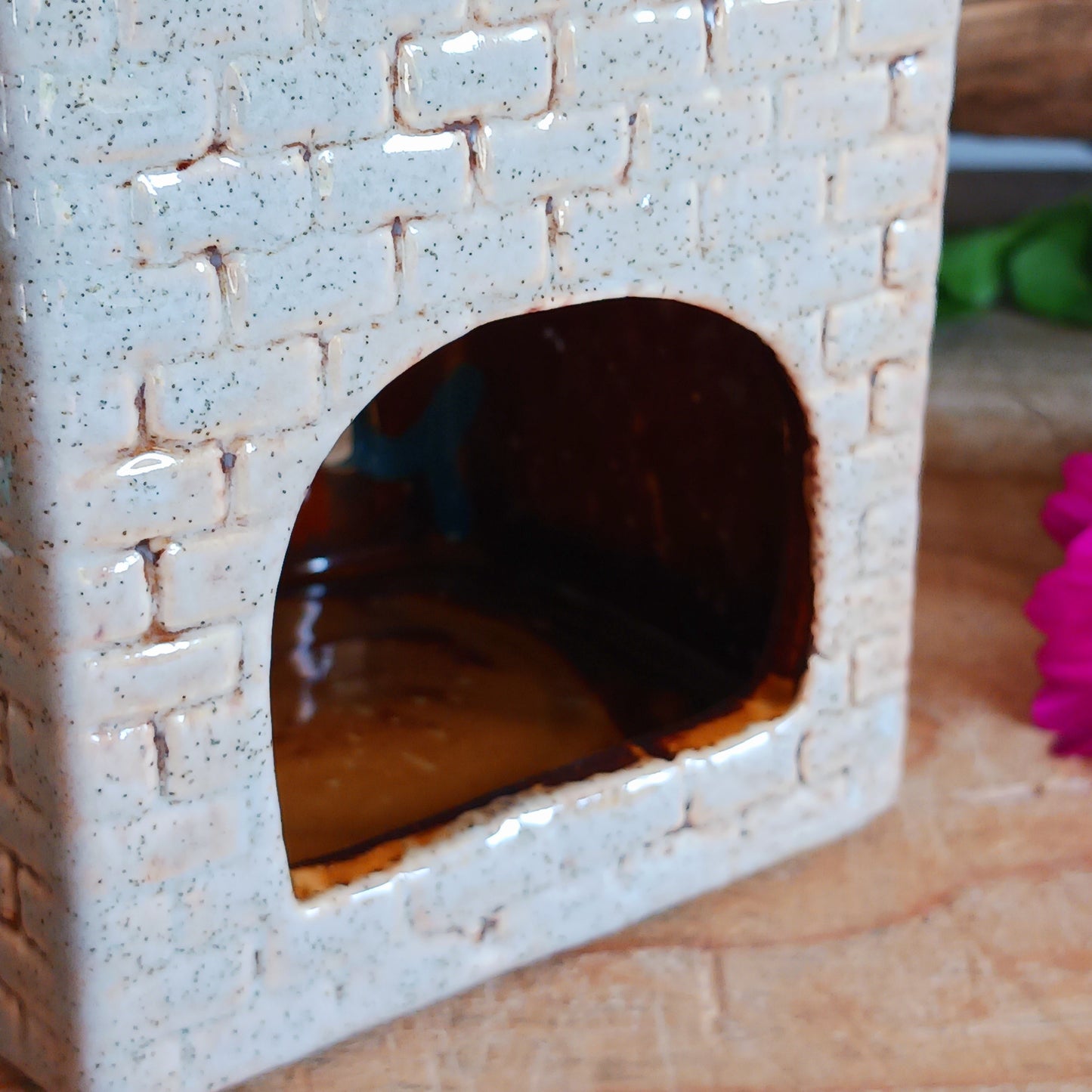 Bring the warmth of a cozy pub into your home with the Village Pottery Crown Pub Tealight. Crafted from ceramic with intricate detailing, this charming piece features a rear cut-out for easy placement of a tealight or string lights. Watch as the soft glow spills through the windows, creating a welcoming pub atmosphere. Perfect for building your own enchanting village display, this timeless decoration adds warmth and character to any space.