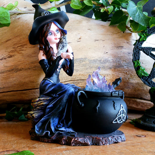Meet Alvina, a captivating hand-painted witch figurine seated peacefully on a rustic log with her enchanting owl companion. Dressed in a flowing blue gown with long brown hair, Alvina has a mysterious yet charming presence that will appeal to lovers of witches, fantasy and magical décor.