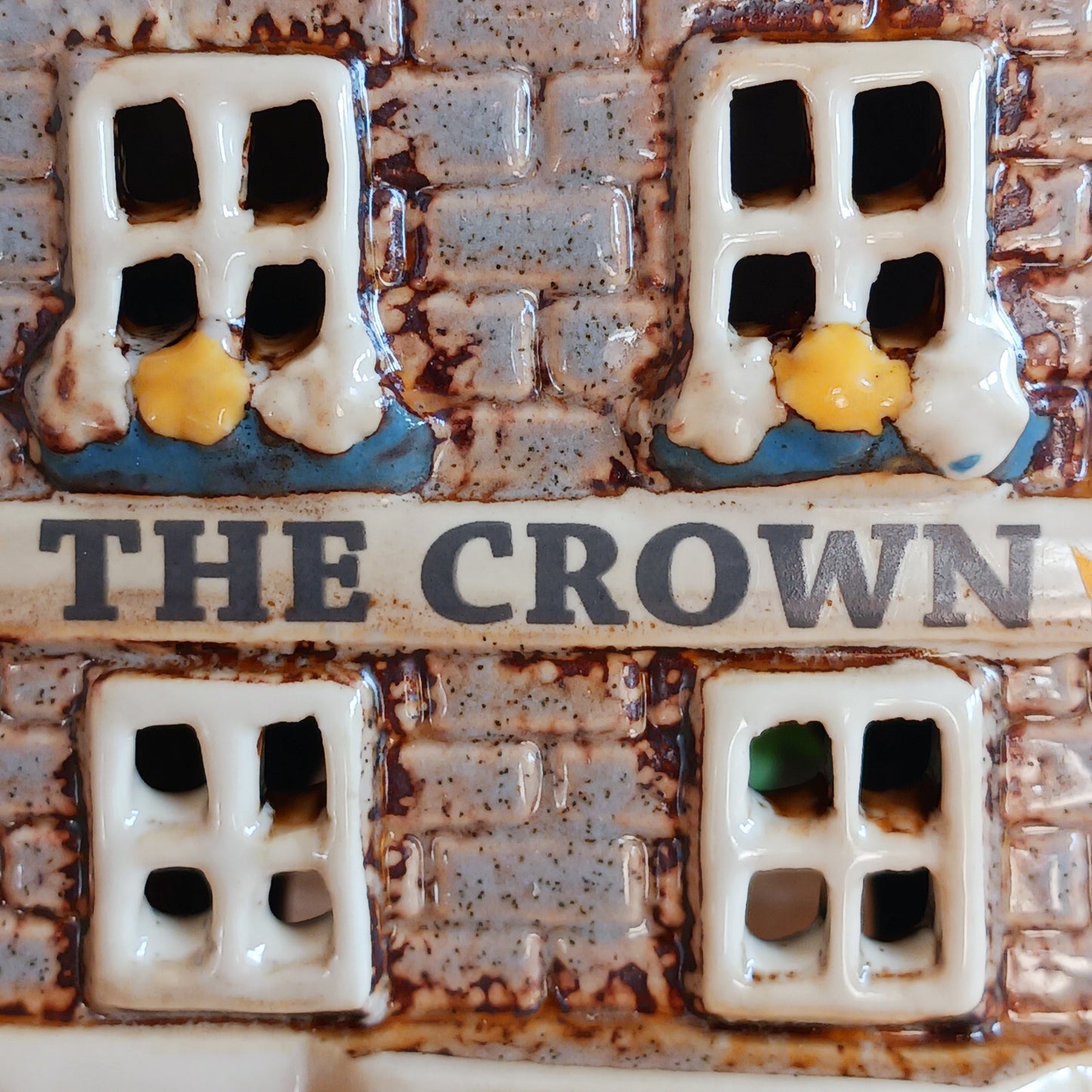 Bring the warmth of a cozy pub into your home with the Village Pottery Crown Pub Tealight. Crafted from ceramic with intricate detailing, this charming piece features a rear cut-out for easy placement of a tealight or string lights. Watch as the soft glow spills through the windows, creating a welcoming pub atmosphere. Perfect for building your own enchanting village display, this timeless decoration adds warmth and character to any space.