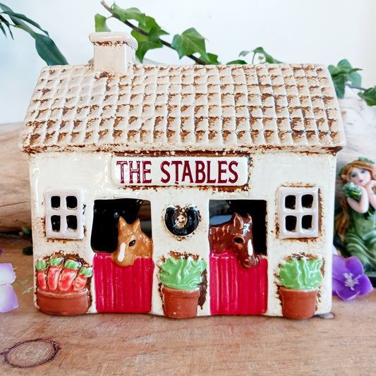 Nestled at the edge of a quiet enchanted village, The Stables tealight house by Village Pottery glows with a soft, grounding warmth. Crafted from ceramic and measuring 17x8x8cm, this rustic stable invites candlelight to flicker through its windows like a lantern for wandering spirits and kindred souls.