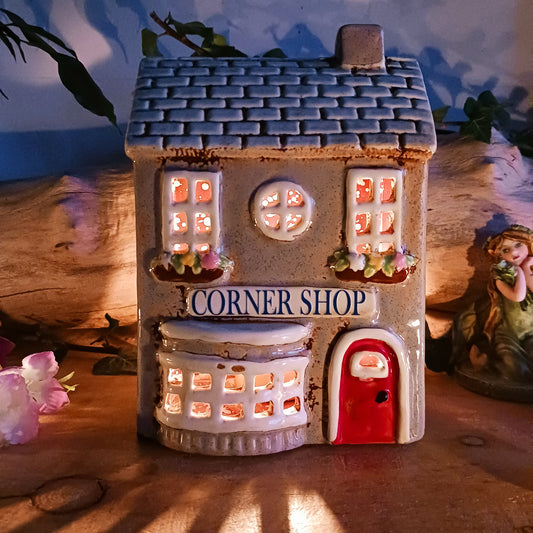 At the heart of an enchanted street stands the Corner Shop, its windows glowing softly as if lit by unseen hands. This Shudehill Village Pottery tealight house is crafted from ceramic to capture the quiet magic of village life, where candlelight flickers like whispered exchanges between worlds.