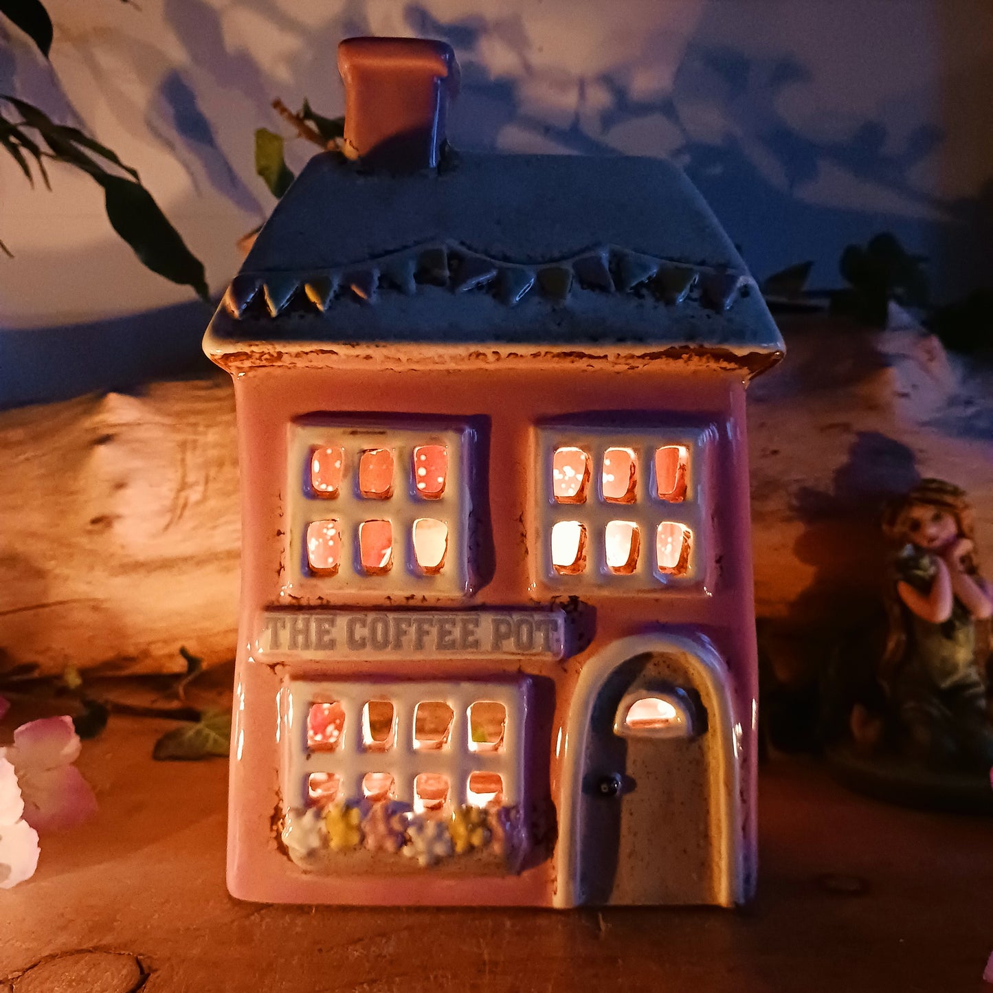 A comforting glow brews within the Coffee Pot Shop, where candlelight flickers like steam rising from a warm cup in a quiet enchanted village. This Shudehill Village Pottery tealight house is crafted from ceramic, casting a soft, golden light through its windows to create a scene of calm and gentle magic.