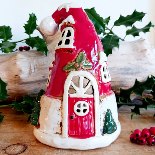 Add a sprinkle of festive cheer to your home with the Village Pottery Christmas Santa Hat House Tealight Holder, a delightful handcrafted ceramic piece full of Christmas magic. Measuring 12 x 12 x 11 cm, this charming little house wears a bright red Santa hat for a roof, capturing the warmth and whimsy of the season in perfect detail.